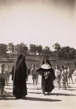 Photo showing two nuns in the foreground and young boys in the background