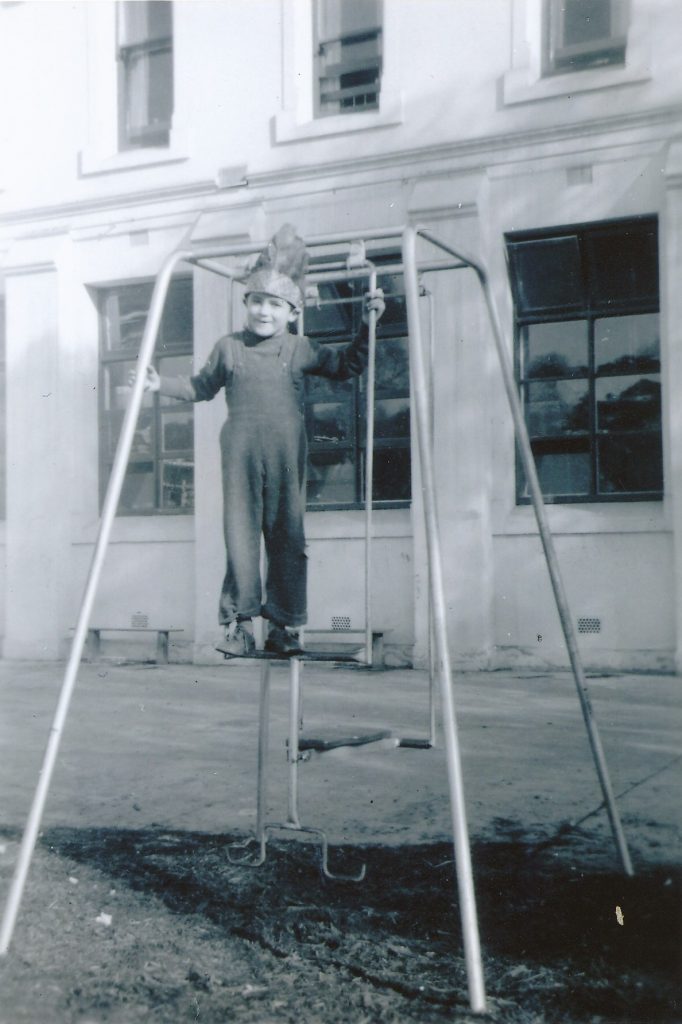 Black and white photograph of a young boy standing on a swing.