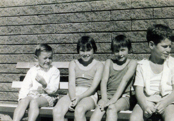 Group of four children sitting on a bench against a wall